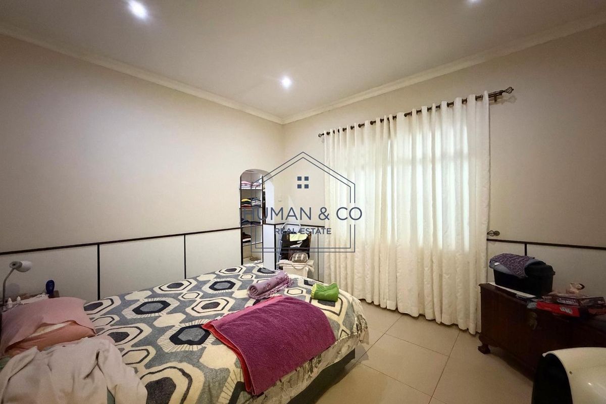 A bedroom featuring tiled flooring, recessed downlighting, and built-in wall paneling, with a window dressed in curtains.