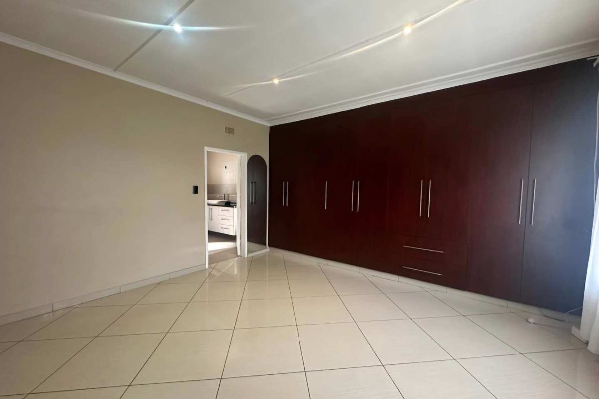 Spacious bedroom featuring extensive dark wood built-in cupboards, neutral wall finishes, and large format floor tiles.