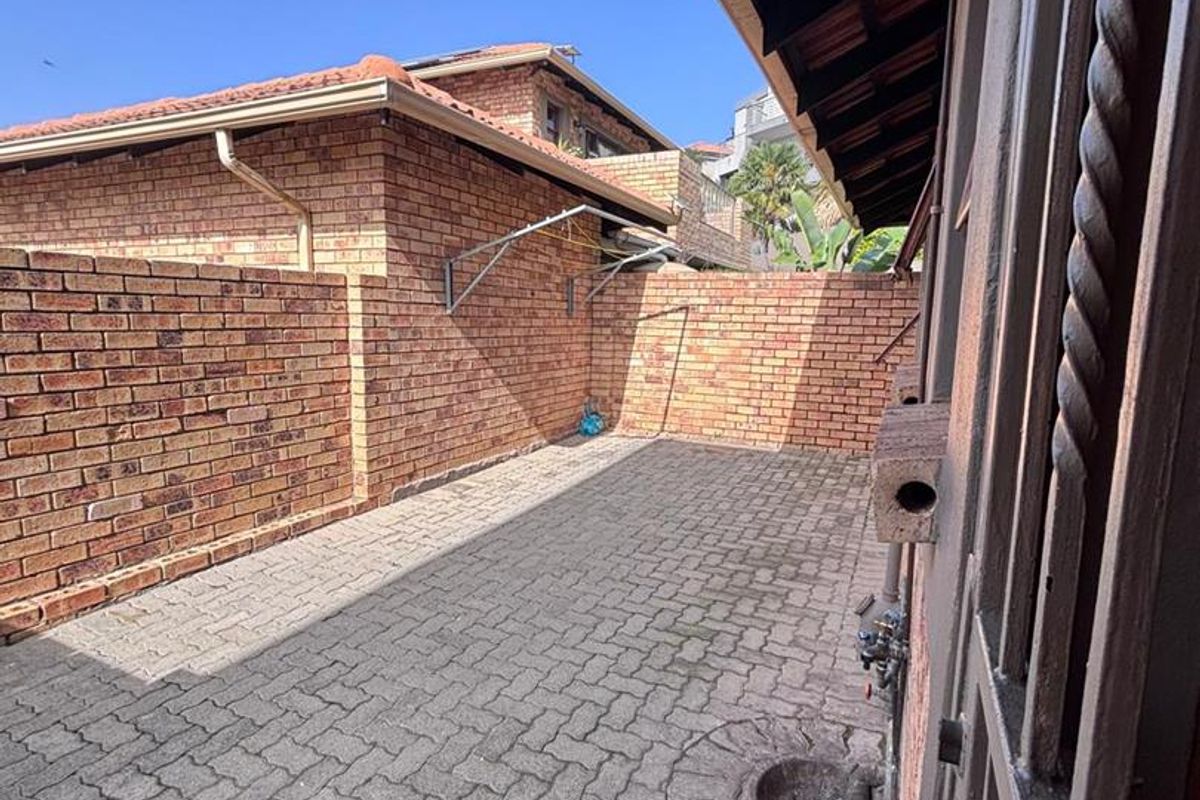 A private rear courtyard area featuring brick boundary walls, paved flooring, and a wall-mounted drying rack.