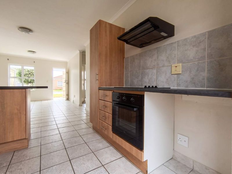 A functional kitchen featuring built-in cabinetry, oven, hob, and extractor fan, with tiled flooring and a neutral backsplash, leading into an open-plan living area.