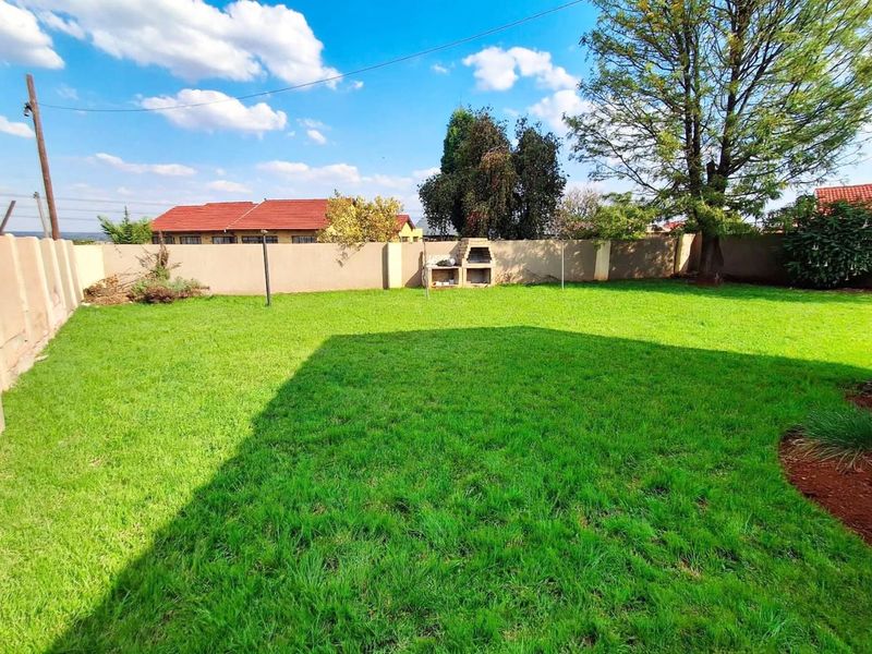 A spacious, well-maintained backyard featuring a lush green lawn, perimeter boundary walls, and a built-in outdoor braai area.