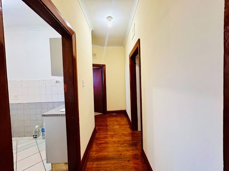 A narrow hallway featuring original hardwood flooring and timber door frames, providing access to adjacent rooms including a tiled kitchen area.