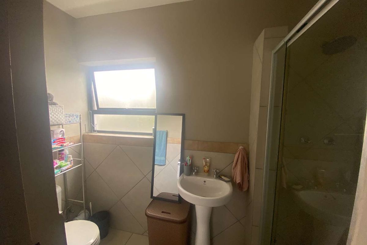 A functional bathroom featuring a pedestal basin, toilet, and a glass-enclosed shower with neutral wall and floor tiling.