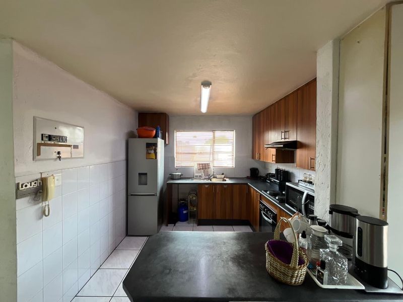 A functional kitchen featuring wood-finish cabinetry, laminate countertops, tiled splashbacks, and ceramic flooring, offering a practical layout for daily meal preparation.