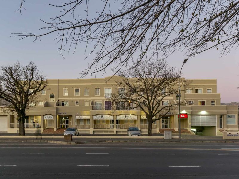 Front elevation of a multi-story apartment building featuring ground floor commercial units, balconies, and secure street-level parking access.