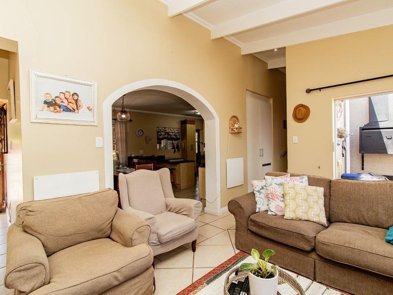A living room featuring exposed timber ceiling beams, tiled flooring, and an arched transition to the adjacent kitchen area.