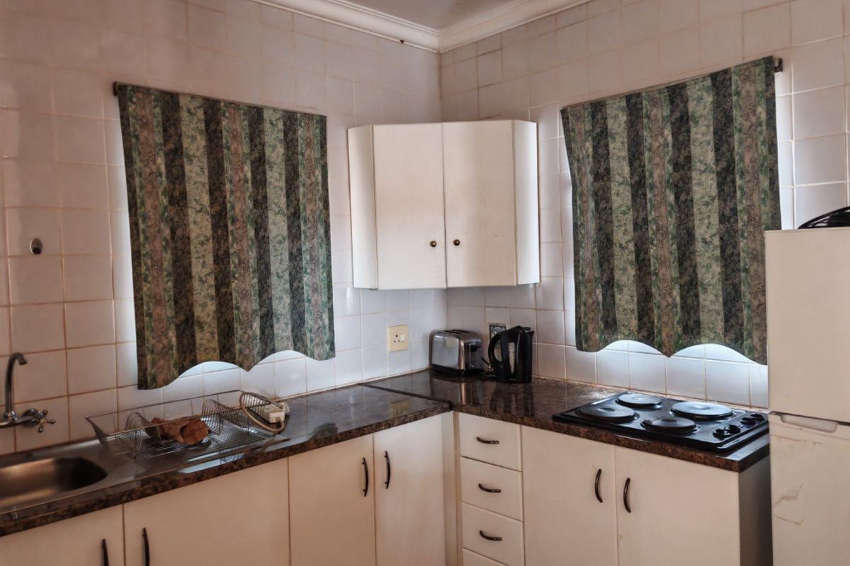 A functional kitchen featuring white cabinetry, dark laminate countertops, a built-in electric hob, and a stainless steel sink with tiled splashbacks.