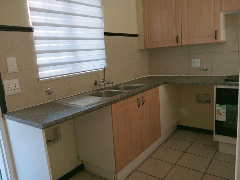 A functional kitchen featuring laminate cabinetry, granite-look countertops, a stainless steel double sink, and a built-in oven with tiled flooring.