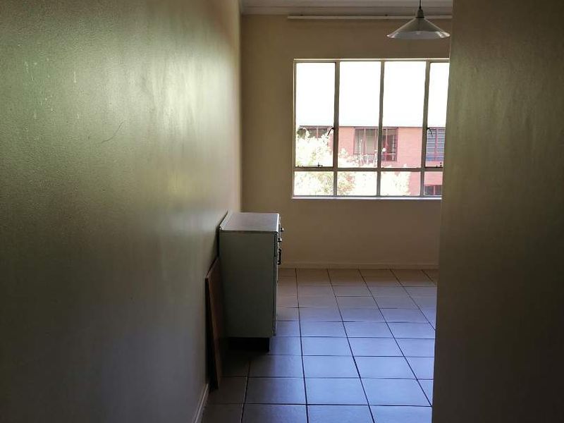 An empty living area featuring tiled flooring, a large window providing natural light, and a simple pendant light fixture.