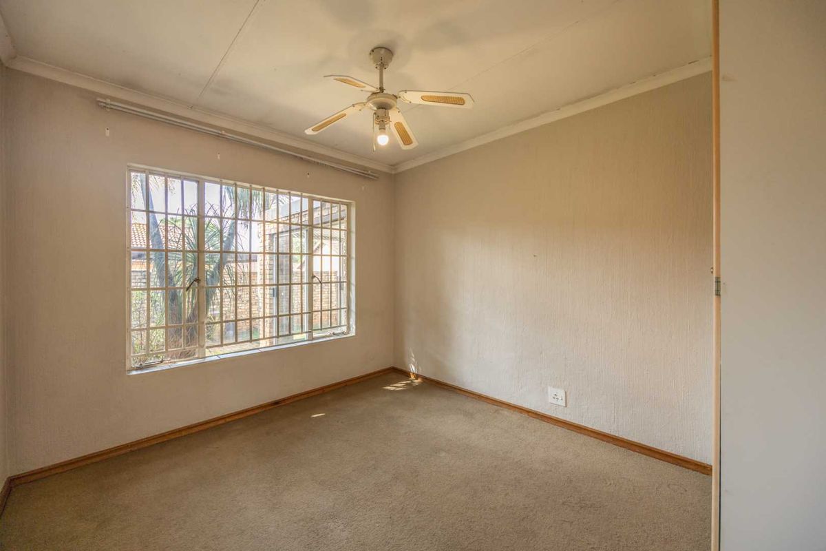 An empty bedroom featuring a ceiling fan, built-in cupboard, and large window with security bars, offering a blank canvas for renovation.