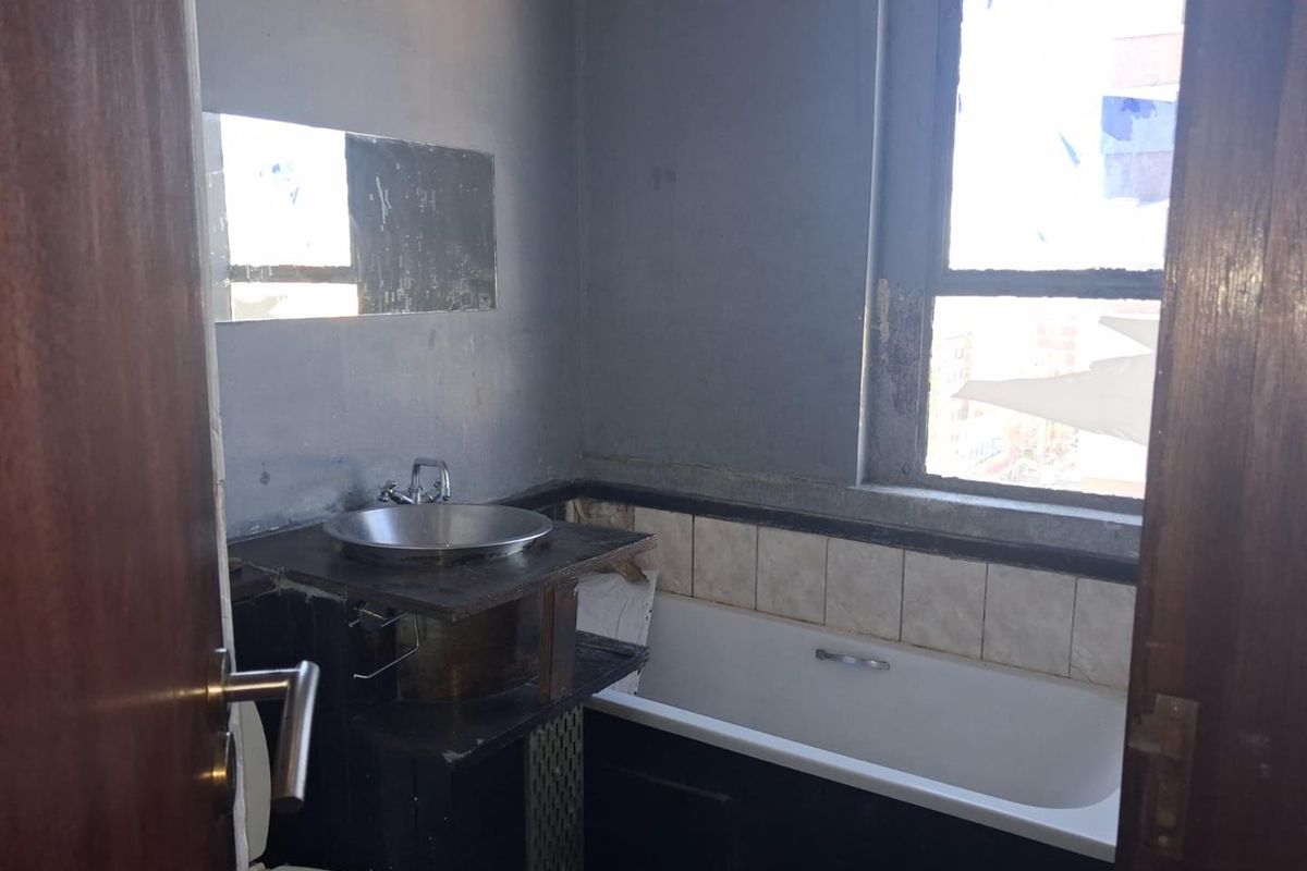 A dated bathroom featuring a bathtub, vessel sink, and wall mirror, requiring significant renovation and cosmetic updates to improve its condition.