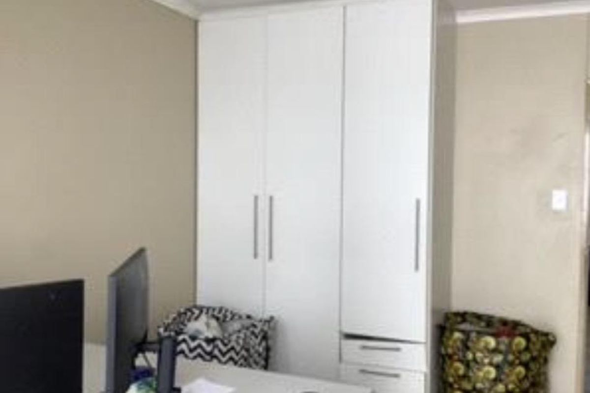 A bedroom featuring a clean, white built-in wardrobe with integrated drawers and classic ceiling coving.