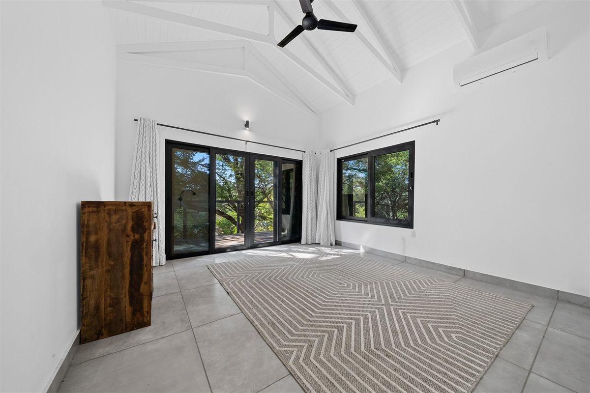 Bright living room featuring a vaulted ceiling with exposed rafters, tiled flooring, split-system air conditioning, and large sliding glass doors opening to the outdoors.