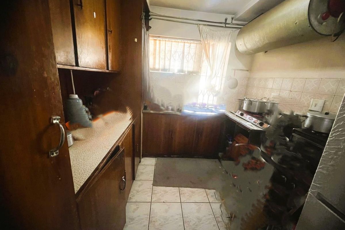 A dated kitchen featuring original wooden cabinetry, tiled backsplash, and tiled flooring, requiring modernization to improve functionality and aesthetic appeal.