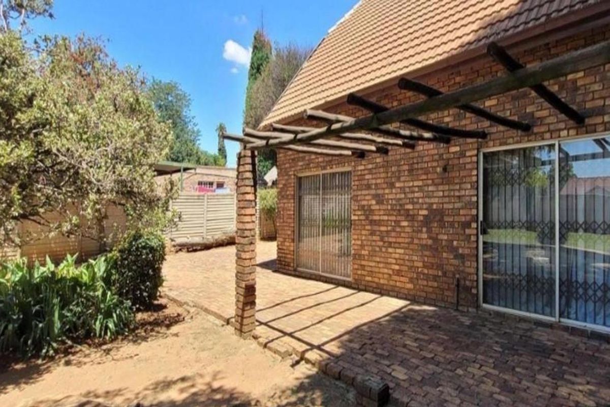 Rear exterior view featuring a brick-paved patio area with a timber pergola, brick facade, and sliding glass doors with security gates.