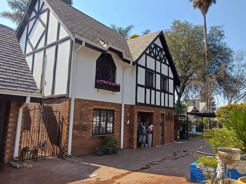 A charming Tudor-style house featuring a brick and timber-framed facade, a tiled roof, and a paved driveway leading to an attached garage.
