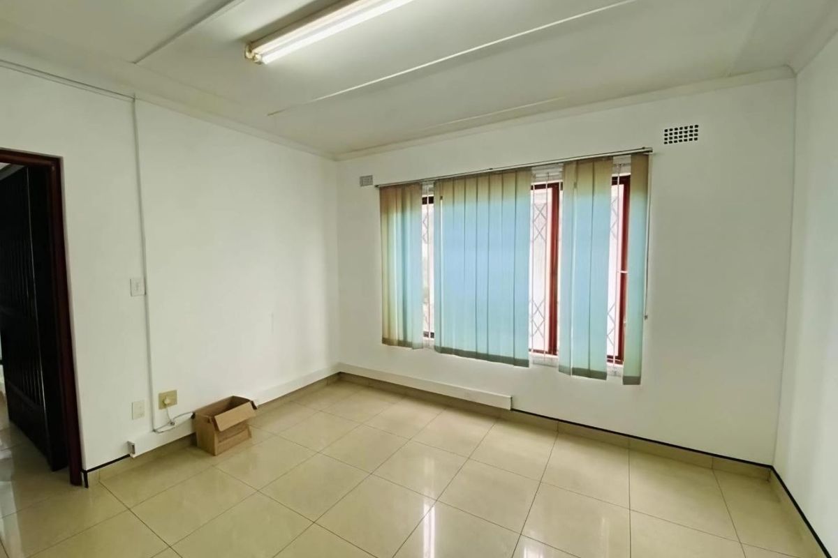 A vacant bedroom featuring neutral tiled flooring, large windows with security bars, and vertical blinds, offering a clean canvas for personalization.