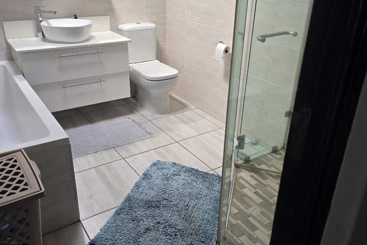 Modern bathroom featuring a floating vanity, vessel sink, separate glass-enclosed shower, and a bathtub with neutral floor-to-ceiling tiling.