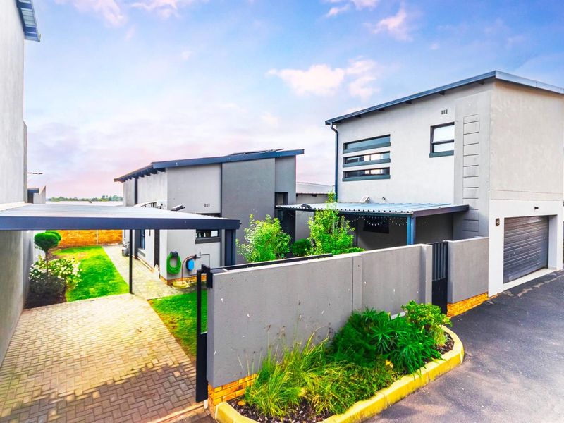 Modern townhouse exterior featuring a paved driveway, carport, attached garage, and well-maintained garden area with boundary walling.