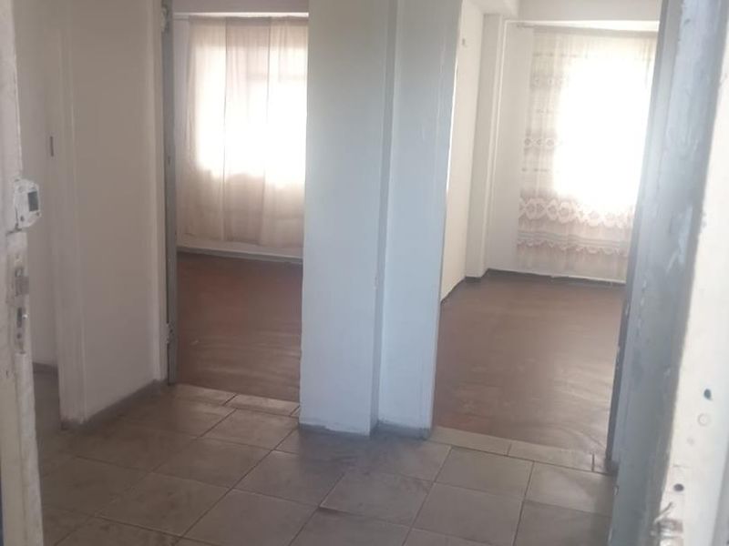 A vacant hallway with tiled flooring providing access to two adjacent rooms with natural light.