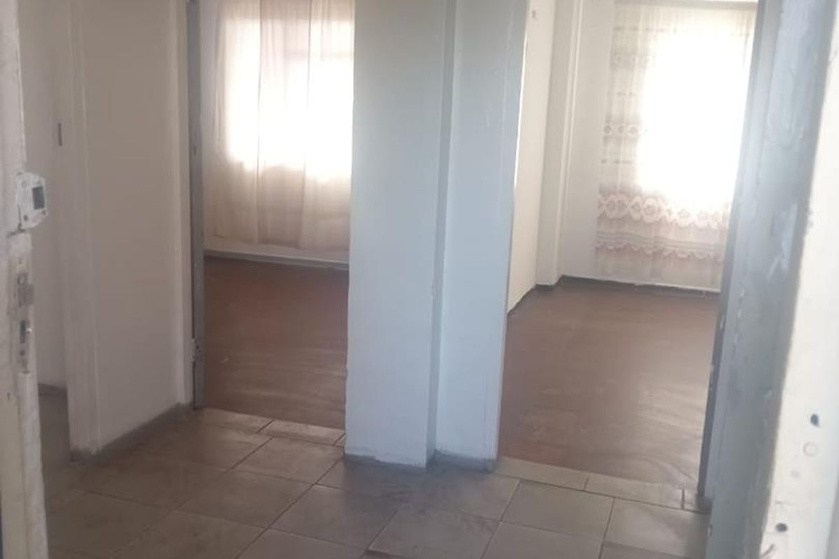 A vacant hallway with tiled flooring providing access to two adjacent rooms with natural light.