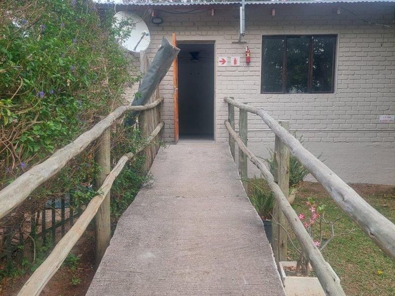 Exterior view of a building entrance featuring a concrete access ramp with timber handrails and a painted brick facade.