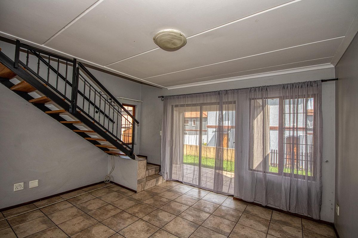 Open plan living area featuring tiled flooring, a metal staircase, and sliding glass doors providing access to the rear patio and garden.