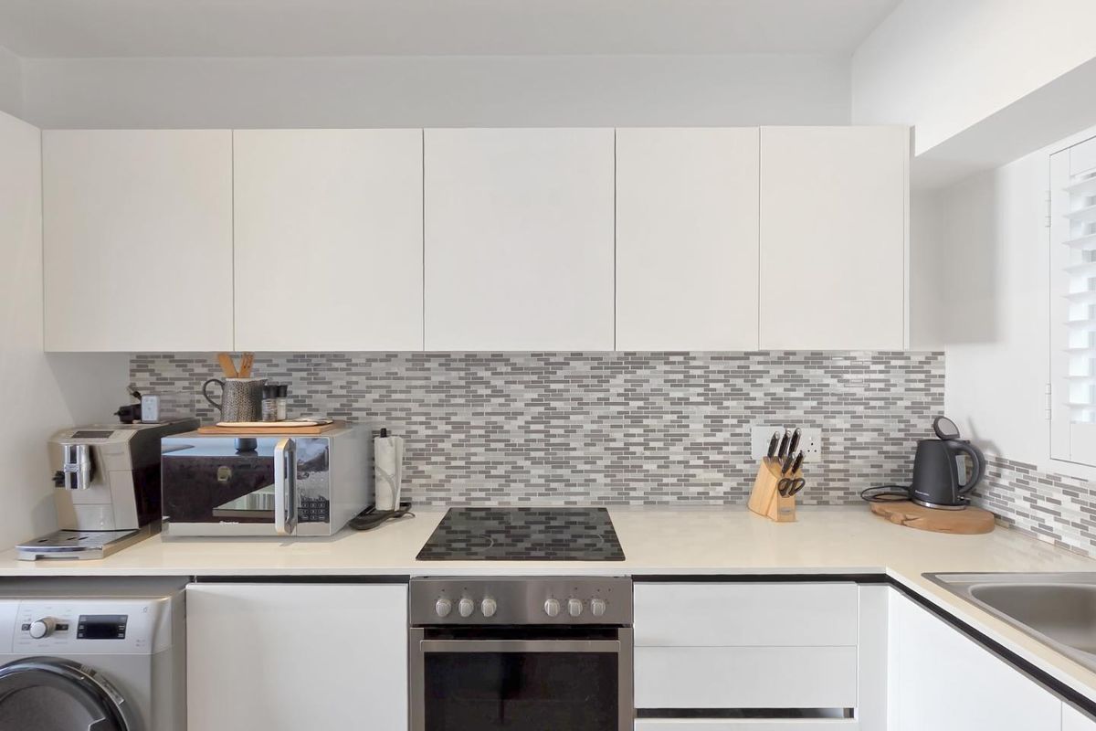 Modern kitchen featuring white cabinetry, stone countertops, a mosaic tile backsplash, and integrated stainless steel appliances.