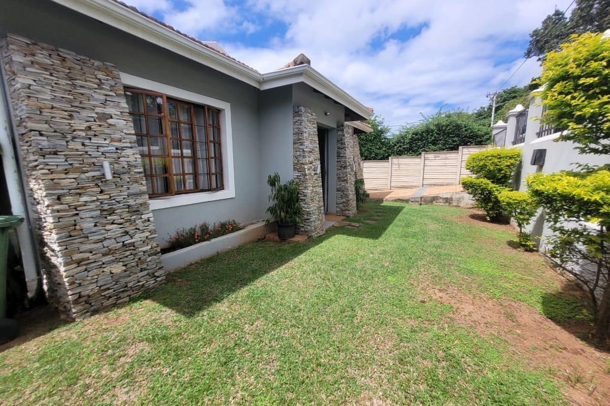 A well-maintained rear exterior view of the house featuring stone cladding accents, timber-framed windows, and a neat lawn area.