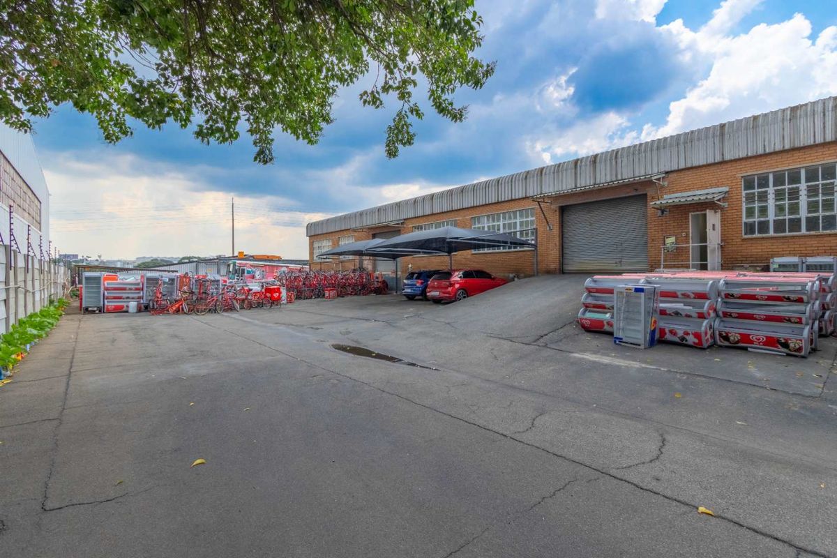 Industrial property exterior featuring a large paved yard, multiple roller shutter access points, and covered parking bays.