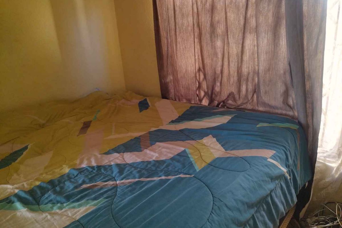 A bedroom featuring a window with curtains, showing signs of wear on the wall finishes.