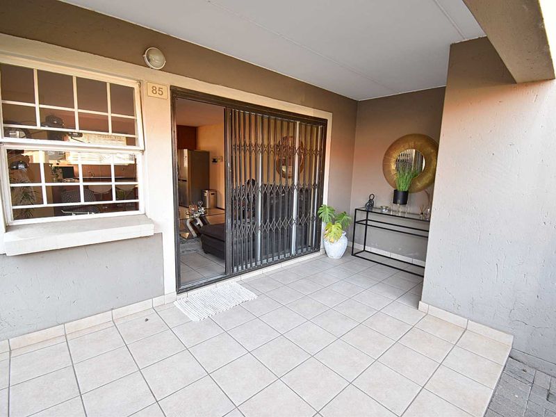 Covered patio area featuring tiled flooring, a sliding glass door with a security gate, and an adjacent window with burglar bars.