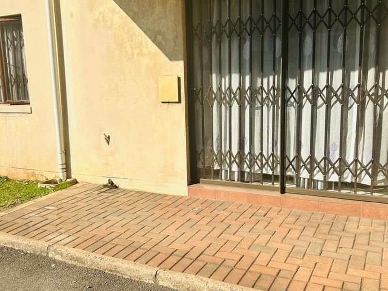 Exterior view of an apartment entrance featuring a paved patio area, sliding glass door with security gate, and weathered exterior wall finishes.