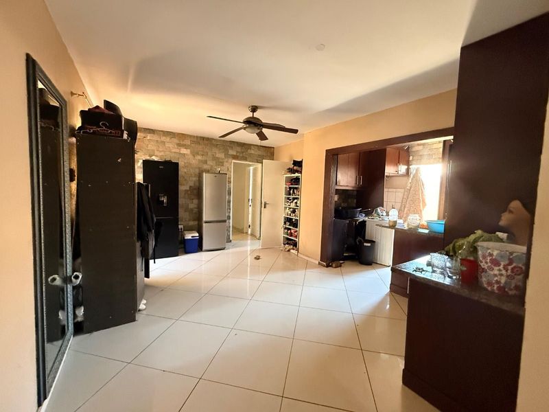 Open-plan living and kitchen area featuring tiled flooring, a ceiling fan, and a stone feature wall, offering a functional layout for daily living.