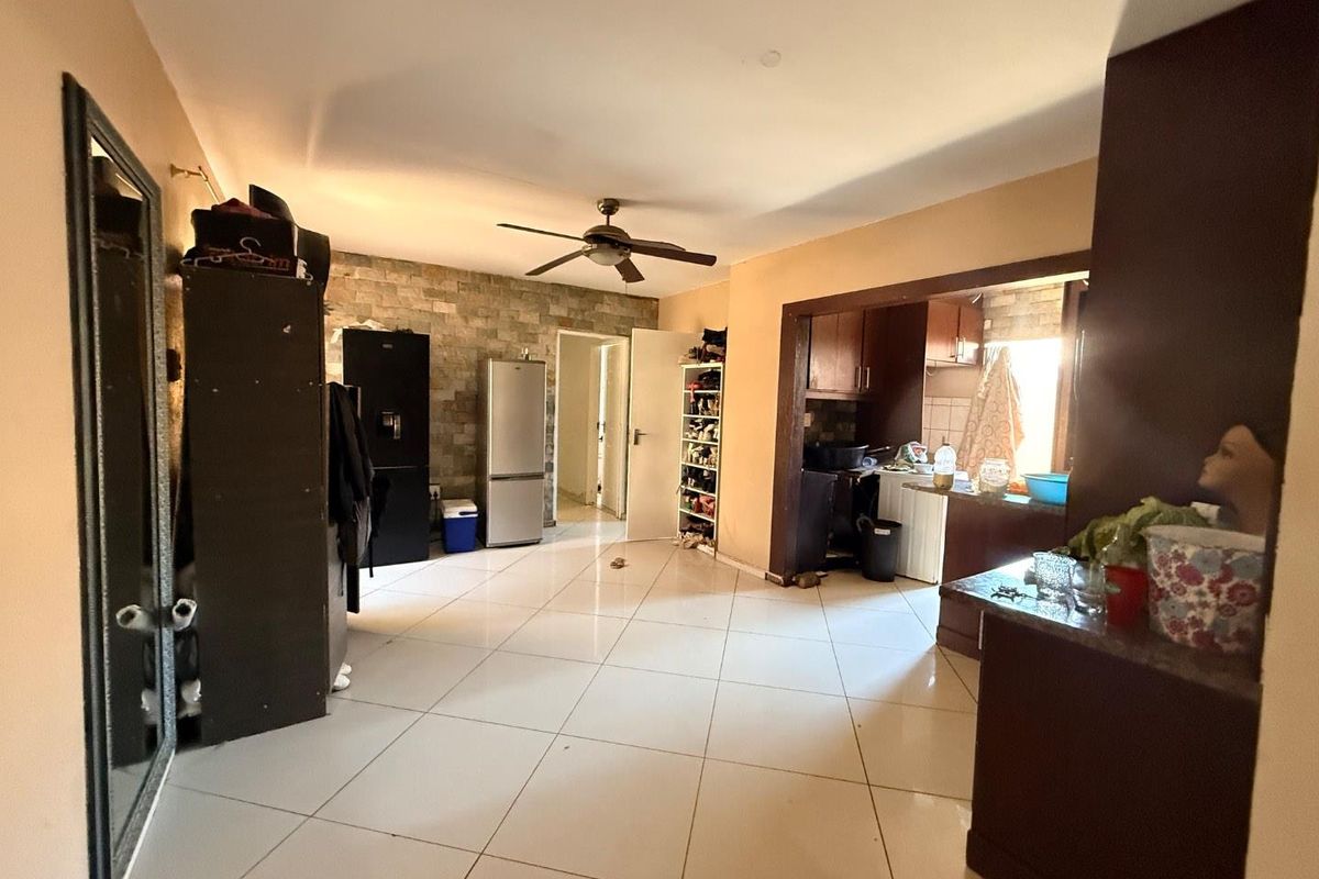 Open-plan living and kitchen area featuring tiled flooring, a ceiling fan, and a stone feature wall, offering a functional layout for daily living.