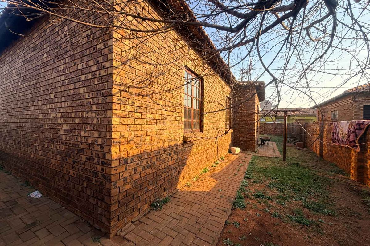 A rear exterior view of the house featuring face brick walls, steel window frames, and a paved walkway leading through the garden area.