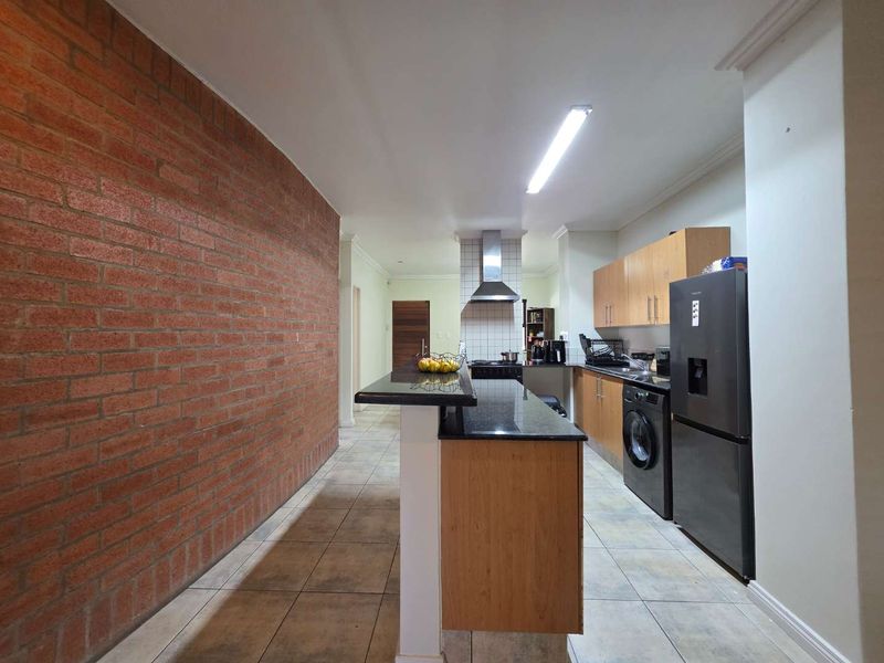 Functional kitchen featuring a breakfast bar, granite countertops, built-in cabinetry, and a distinctive exposed brick feature wall.