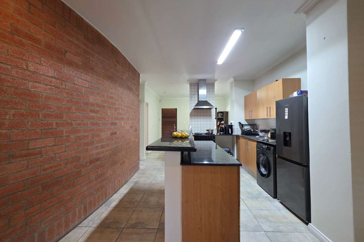Functional kitchen featuring a breakfast bar, granite countertops, built-in cabinetry, and a distinctive exposed brick feature wall.