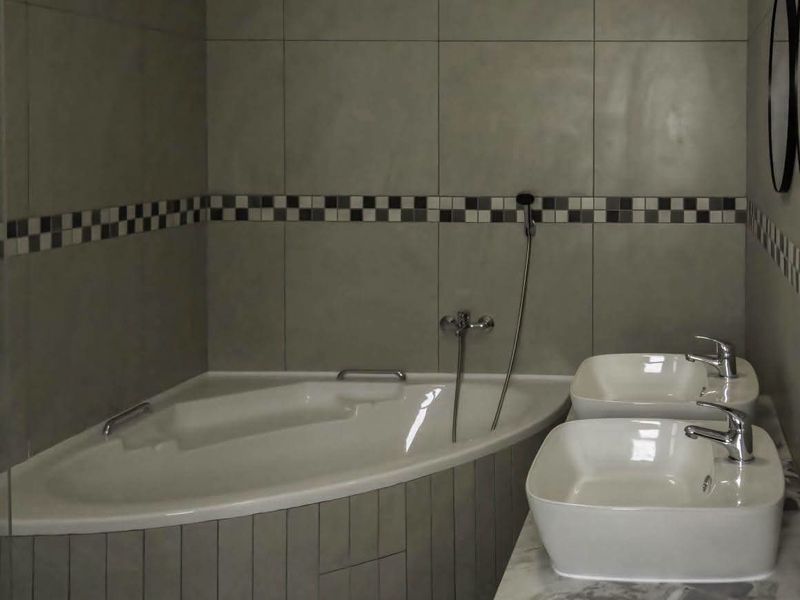 Modern bathroom featuring a corner bathtub, dual vessel sinks on a marble vanity, and stylish grey wall tiling with a mosaic accent border.
