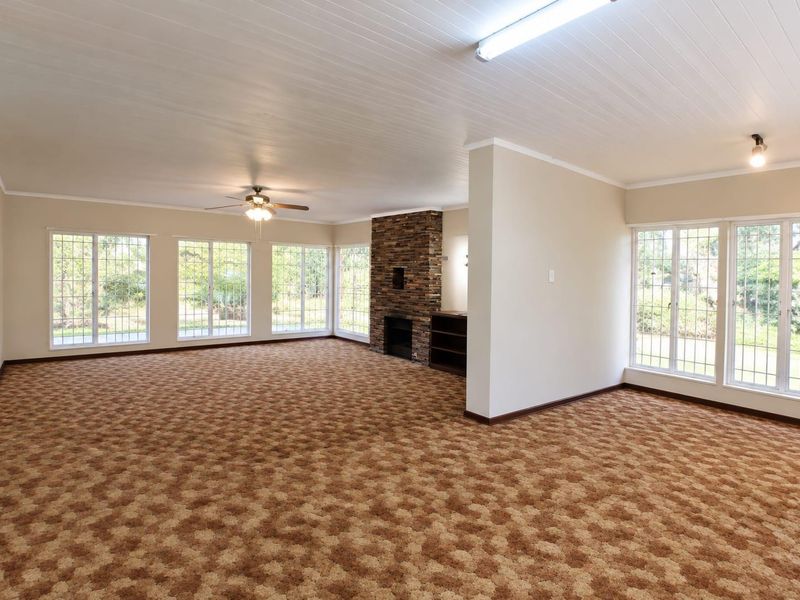 Spacious, light-filled living area featuring a stone fireplace, built-in shelving, and large windows, offering a versatile blank canvas for your interior design vision.