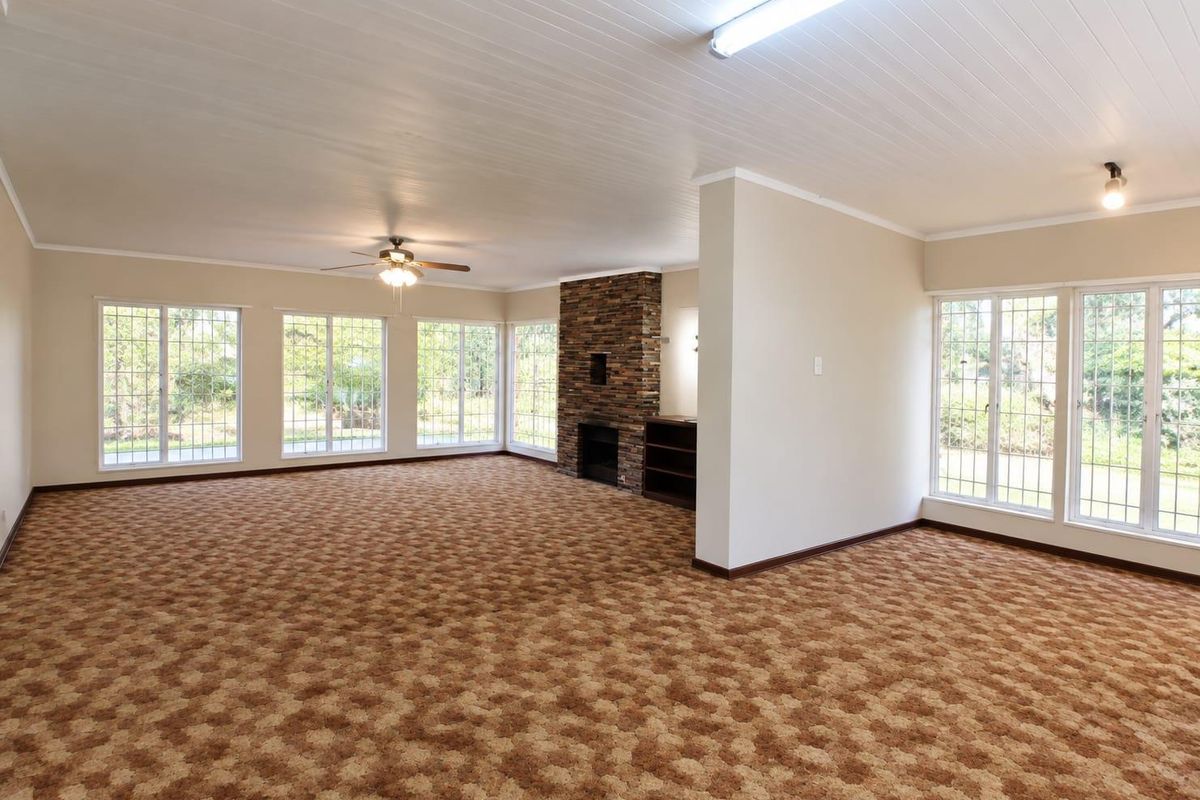 Spacious, light-filled living area featuring a stone fireplace, built-in shelving, and large windows, offering a versatile blank canvas for your interior design vision.