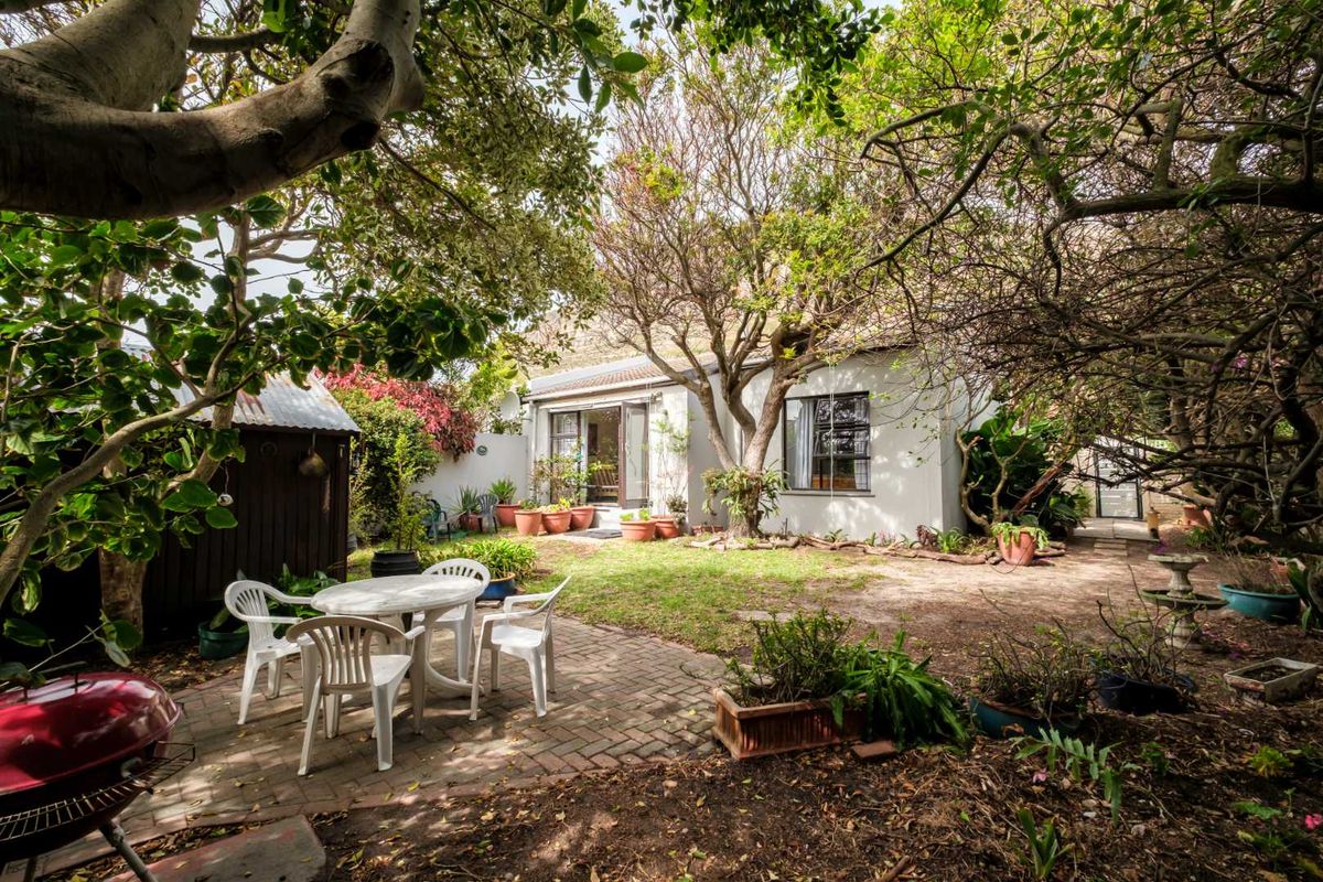 A private rear garden featuring a brick-paved patio area, mature trees, and direct access to the home through sliding glass doors.
