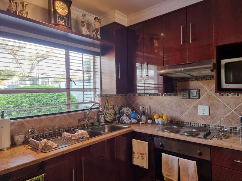 A functional kitchen featuring high-gloss cabinetry, stone countertops, a built-in oven with hob, and a tiled backsplash with a window view.