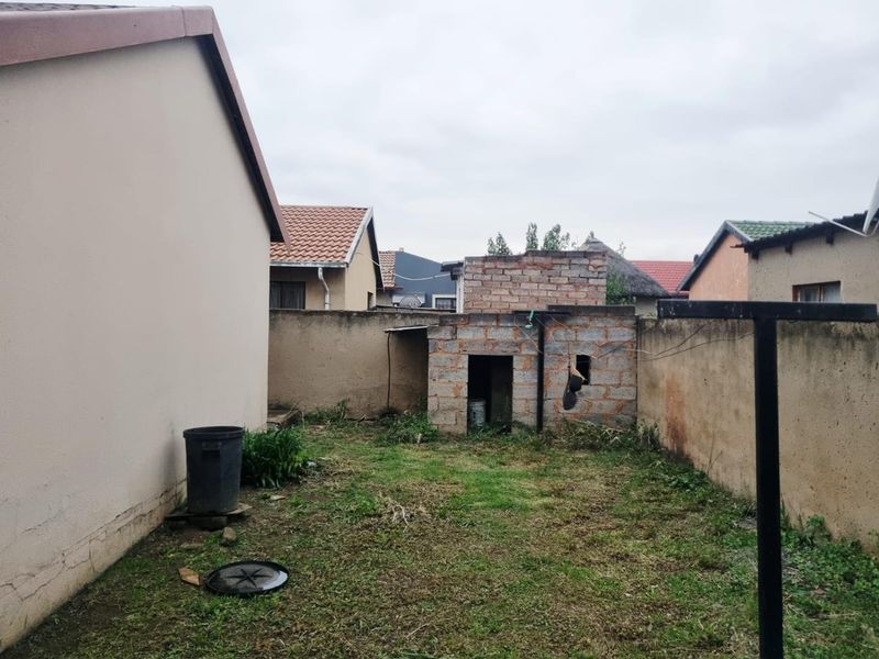 A rear yard area featuring a small unfinished brick outbuilding, boundary walls, and a grassed garden space.
