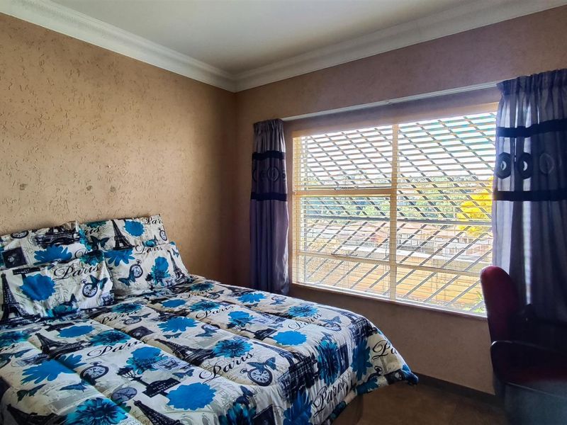 A bedroom featuring textured walls, crown molding, and a window fitted with security bars, offering a functional space with potential for cosmetic updates.