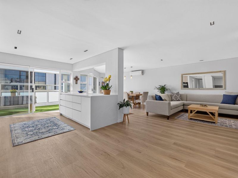 Spacious open-plan living and dining area featuring modern laminate flooring, recessed lighting, and seamless access to a private balcony through large sliding glass doors.