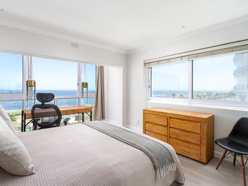 Bright and spacious bedroom featuring large windows with expansive ocean views, neutral finishes, and recessed ceiling lighting.