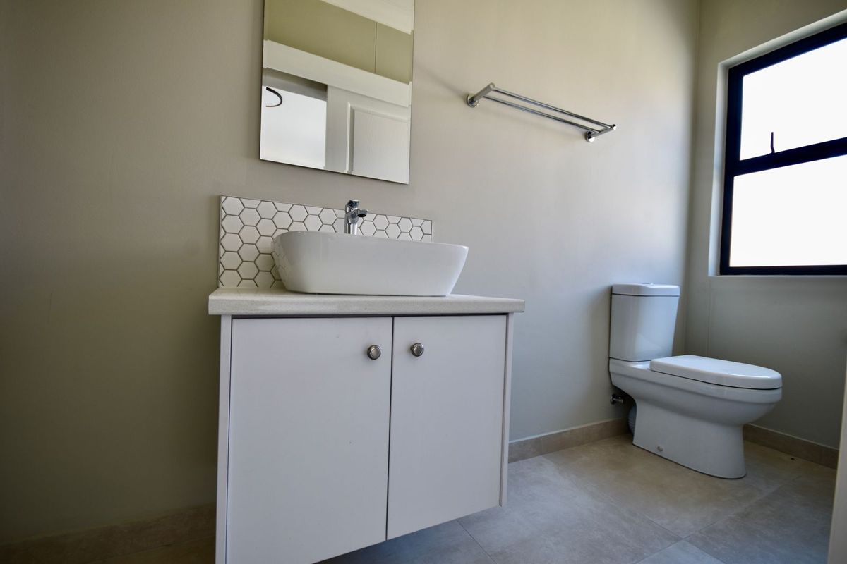 A clean, modern bathroom featuring a vessel sink on a vanity cabinet, a tiled backsplash, and a wall-mounted toilet.
