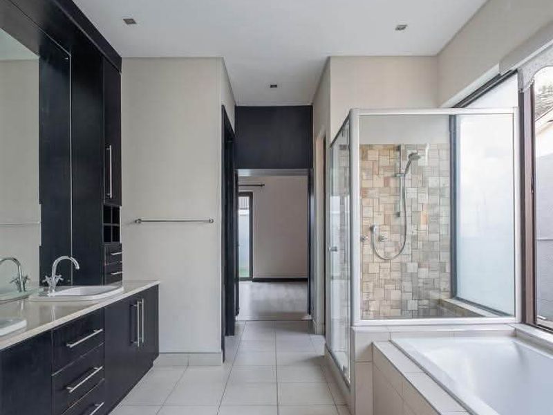 A modern, spacious bathroom featuring a dark wood vanity with double basins, a glass-enclosed shower, and a built-in bathtub with neutral tiled finishes.