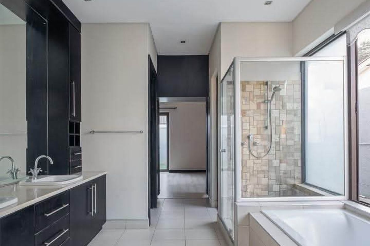 A modern, spacious bathroom featuring a dark wood vanity with double basins, a glass-enclosed shower, and a built-in bathtub with neutral tiled finishes.